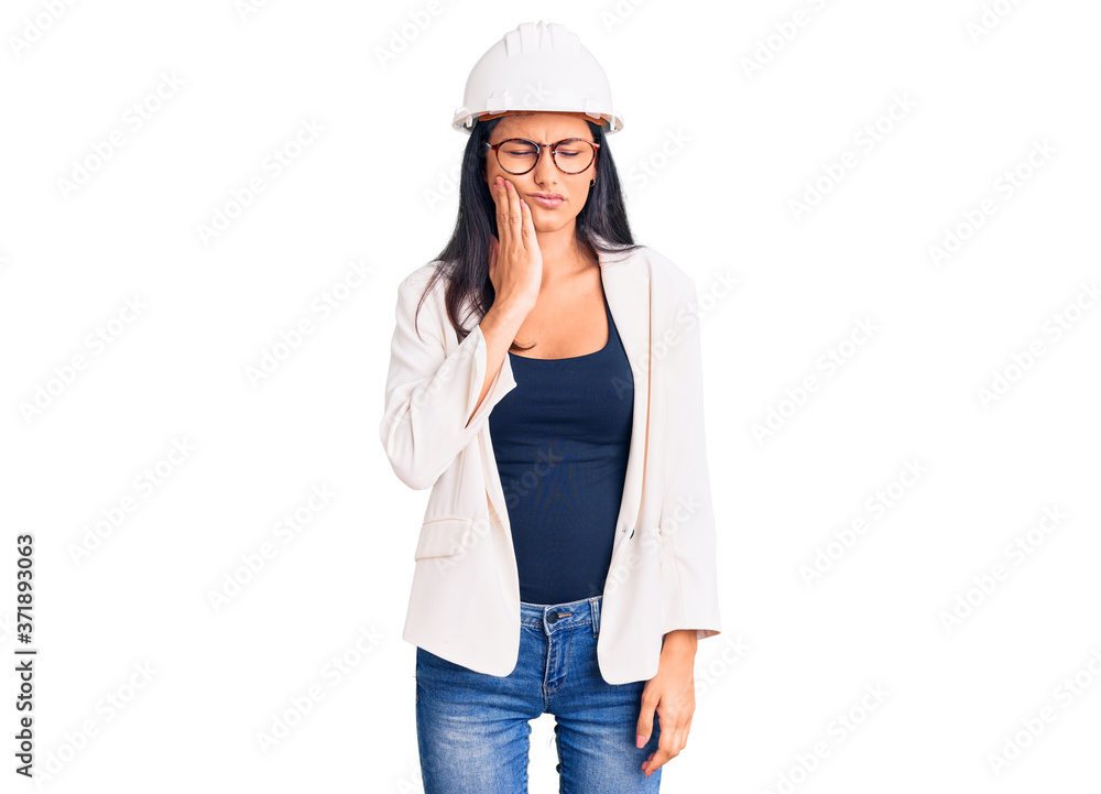 Young beautiful latin girl wearing architect hardhat and glasses touching mouth with hand with painful expression because of toothache or dental illness on teeth. dentist Young beautiful latin girl wearing architect hardhat and glasses touching mouth with hand with painful expression because of toothache or dental illness on teeth. dentist