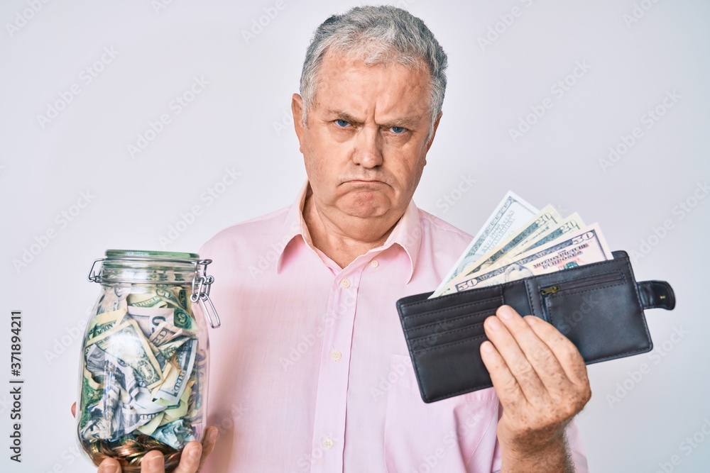 Senior grey-haired man holding wallet with dollars and jar with savings depressed and worry for distress, crying angry and afraid. sad expression. Senior grey-haired man holding wallet with dollars and jar with savings depressed and worry for distress, crying angry and afraid. sad expression.