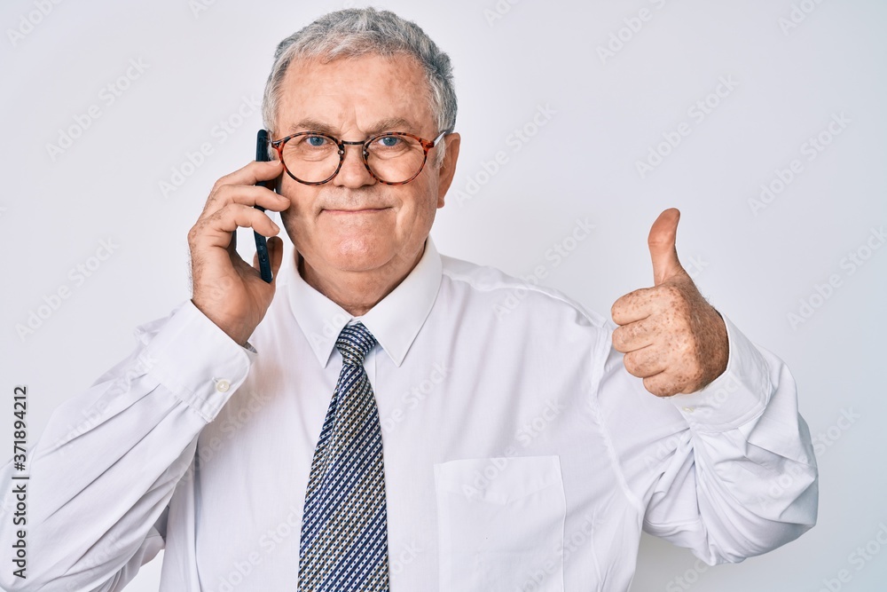 Senior grey-haired man wearing business clothes having conversation talking on the smartphone smiling happy and positive, thumb up doing excellent and approval sign Senior grey-haired man wearing business clothes having conversation talking on the smartphone smiling happy and positive, thumb up doing excellent and approval sign
