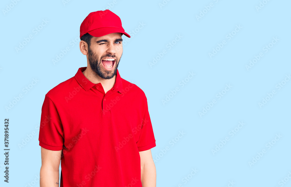 Young handsome man with beard wearing delivery uniform winking looking at the camera with sexy expression, cheerful and happy face.