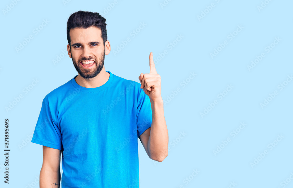 Young handsome man with beard wearing casual t-shirt pointing finger up with successful idea. exited and happy. number one. Young handsome man with beard wearing casual t-shirt pointing finger up with successful idea. exited and happy. number one.