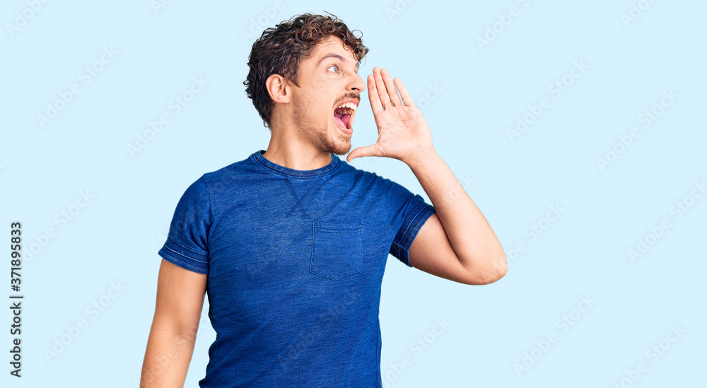 Young handsome man with curly hair wearing casual clothes shouting and screaming loud to side with hand on mouth. communication concept. Young handsome man with curly hair wearing casual clothes shouting and screaming loud to side with hand on mouth. communication concept.