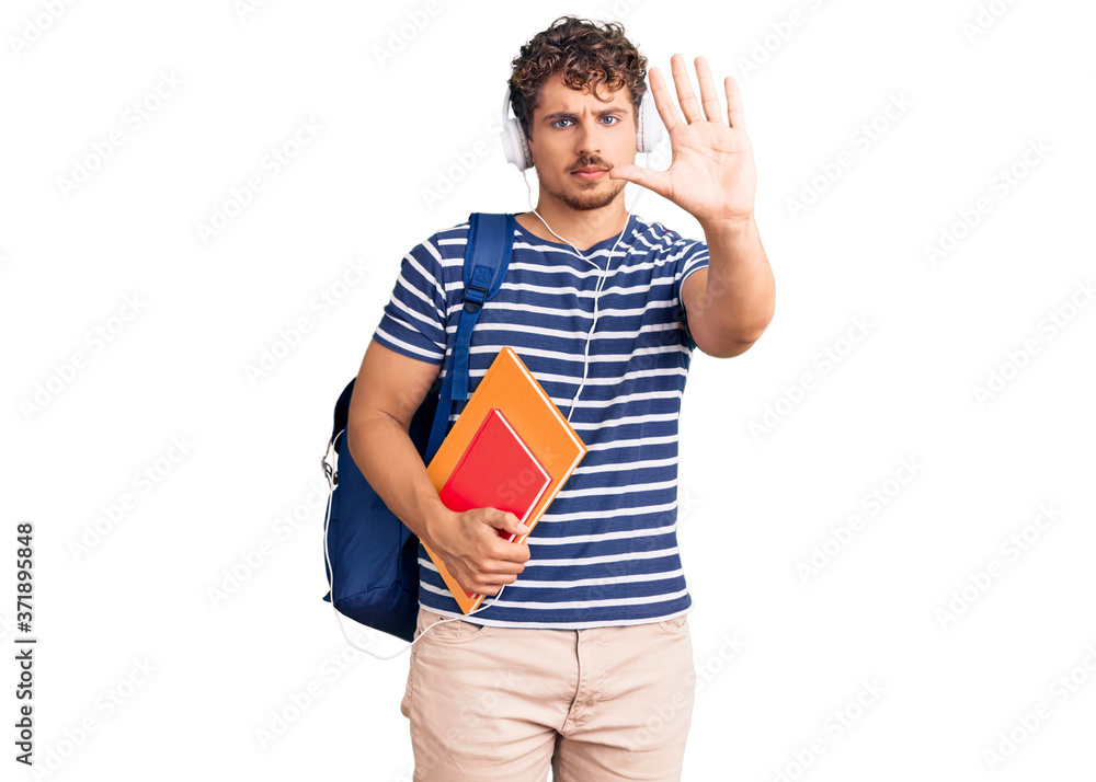 Young handsome man with curly hair holding student backpack and books with open hand doing stop sign with serious and confident expression, defense gesture Young handsome man with curly hair holding student backpack and books with open hand doing stop sign with serious and confident expression, defense gesture