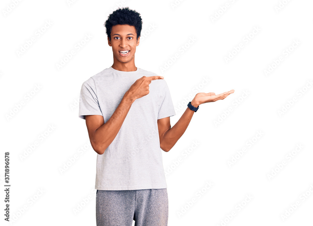 Young african american man wearing casual clothes amazed and smiling to the camera while presenting with hand and pointing with finger. Young african american man wearing casual clothes amazed and smiling to the camera while presenting with hand and pointing with finger.