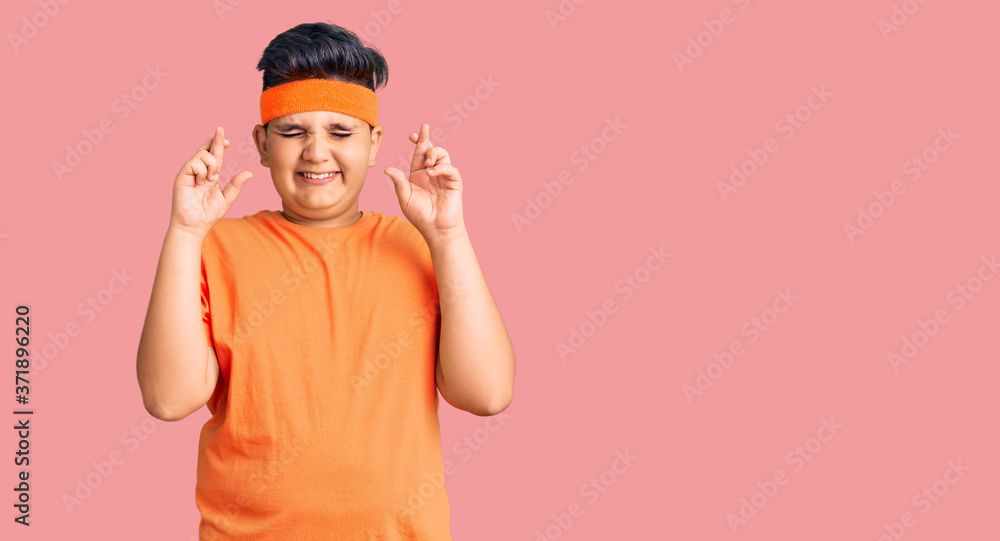 Little boy kid wearing sportswear gesturing finger crossed smiling with hope and eyes closed. luck and superstitious concept. Little boy kid wearing sportswear gesturing finger crossed smiling with hope and eyes closed. luck and superstitious concept.