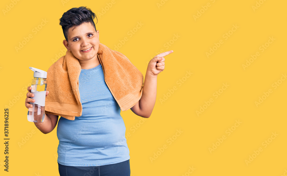Little boy kid wearing sportswear drinking bottle of water smiling happy pointing with hand and finger to the side Little boy kid wearing sportswear drinking bottle of water smiling happy pointing with hand and finger to the side