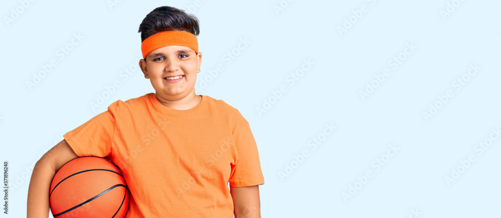 Little boy kid holding basketball ball looking positive and happy standing and smiling with a confident smile showing teeth Little boy kid holding basketball ball looking positive and happy standing and smiling with a confident smile showing teeth
