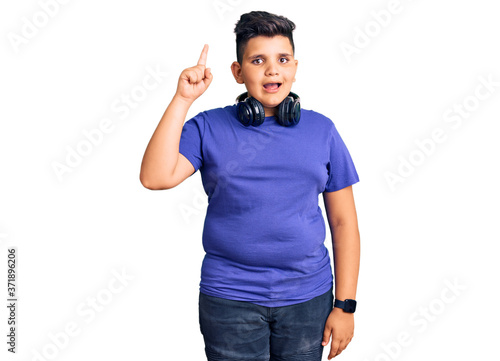 Little boy kid listening to music wearing headphones pointing finger up with successful idea. exited and happy. number one.