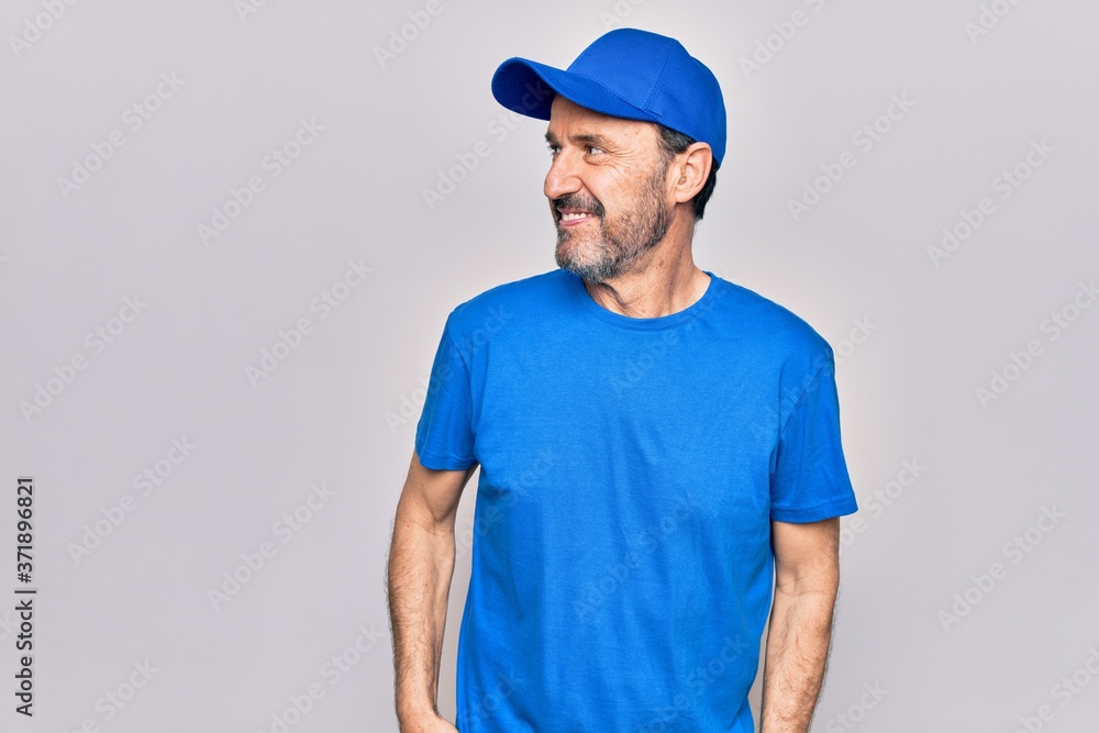Middle age handsome deliveryman wearing cap standing over isolated white background looking to side, relax profile pose with natural face and confident smile.