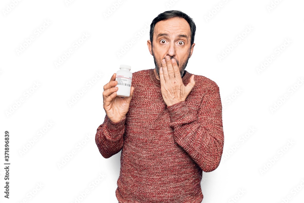 Middle age handsome man holding bottle of medicine pills over isolated white background covering mouth with hand, shocked and afraid for mistake. Surprised expression Middle age handsome man holding bottle of medicine pills over isolated white background covering mouth with hand, shocked and afraid for mistake. Surprised expression