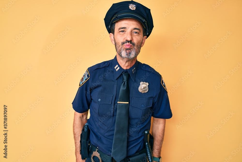 Middle age hispanic man wearing police uniform looking at the camera blowing a kiss on air being lovely and sexy. love expression. Middle age hispanic man wearing police uniform looking at the camera blowing a kiss on air being lovely and sexy. love expression.