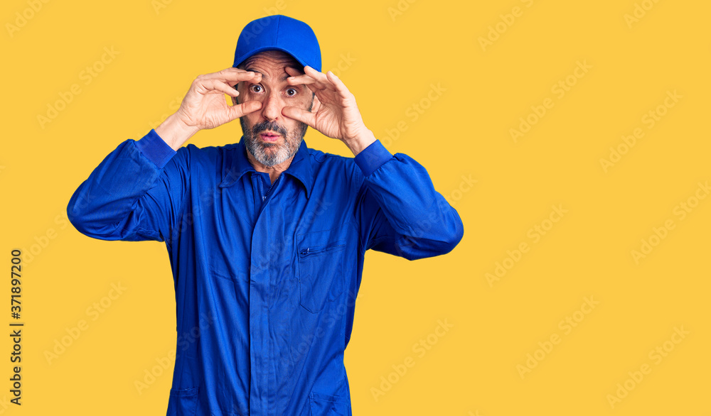 Middle age handsome man wearing mechanic uniform trying to open eyes with fingers, sleepy and tired for morning fatigue