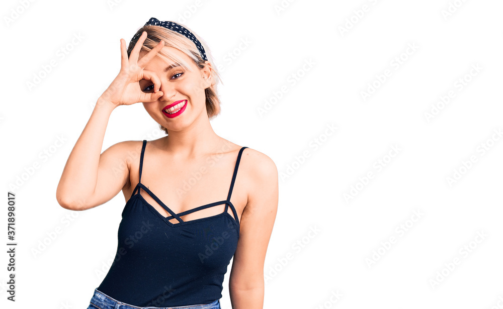 Young beautiful blonde woman wearing casual clothes smiling happy doing ok sign with hand on eye looking through fingers Young beautiful blonde woman wearing casual clothes smiling happy doing ok sign with hand on eye looking through fingers
