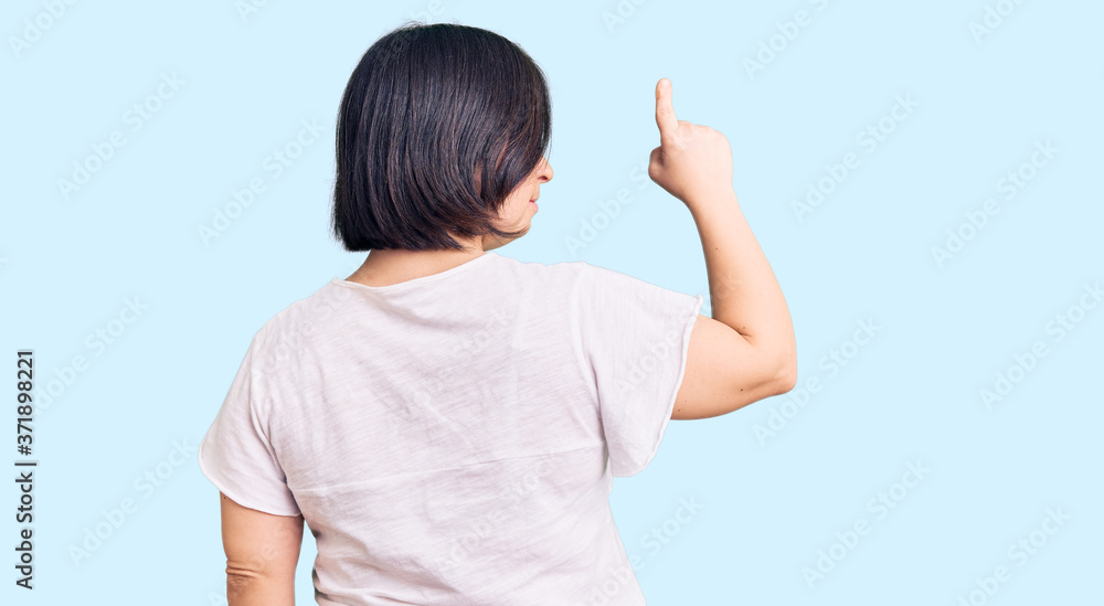 Brunette woman with down syndrome wearing casual white tshirt posing backwards pointing ahead with finger hand Brunette woman with down syndrome wearing casual white tshirt posing backwards pointing ahead with finger hand