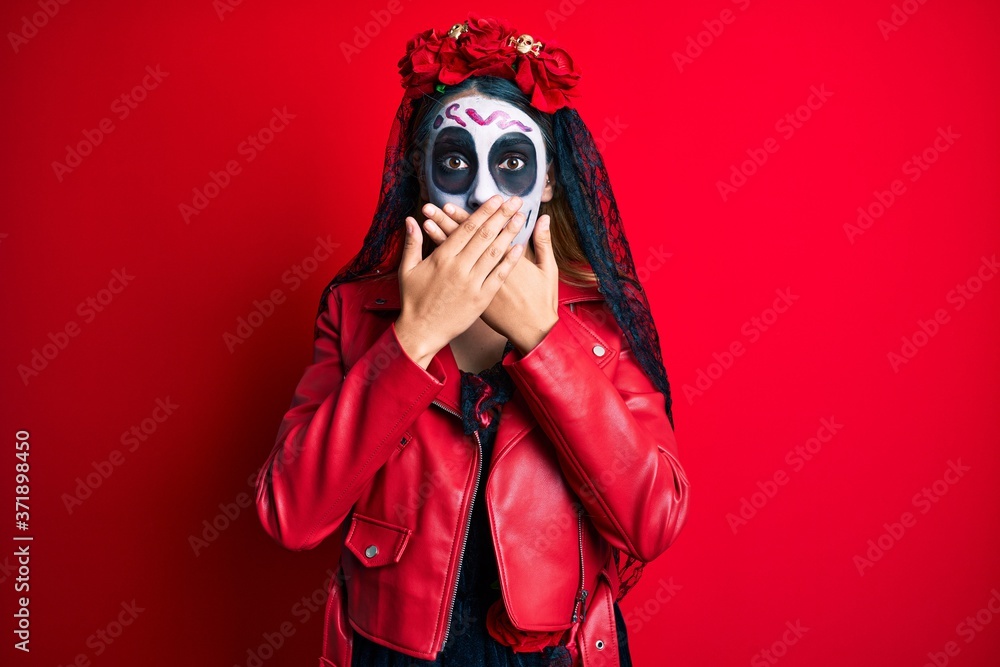 Woman wearing day of the dead costume over red shocked covering mouth with hands for mistake. secret concept. Woman wearing day of the dead costume over red shocked covering mouth with hands for mistake. secret concept.