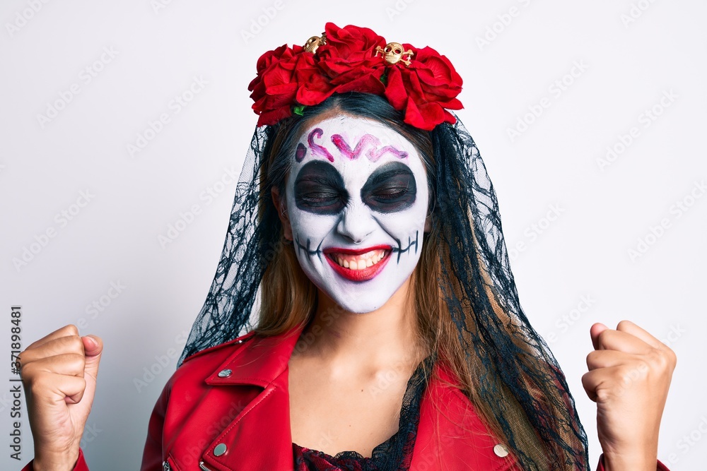 Fototapeta premium Woman wearing day of the dead costume over white very happy and excited doing winner gesture with arms raised, smiling and screaming for success. celebration concept.