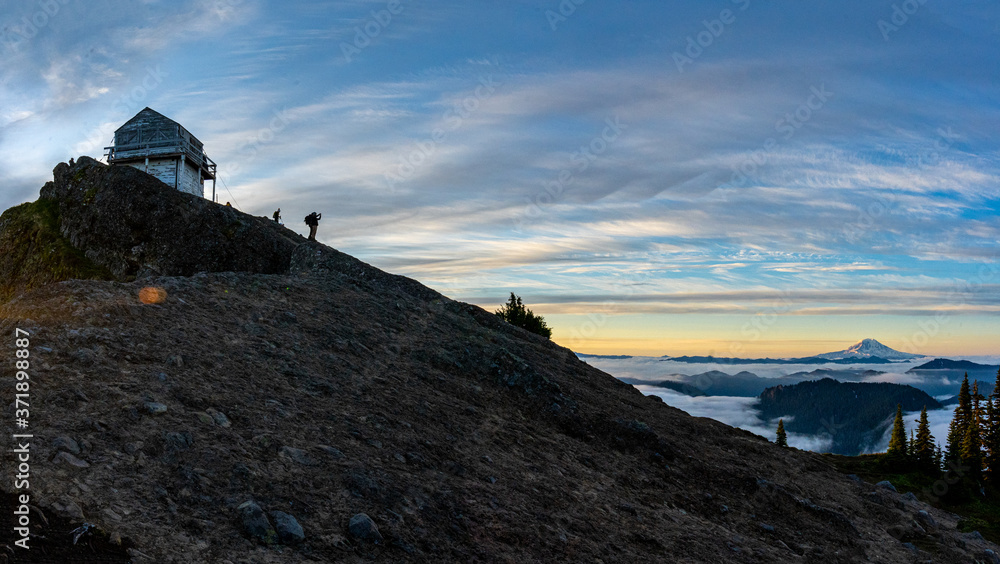 Hikers standing by an old fire lookout watching the sunrise with Mount Hood in the distance