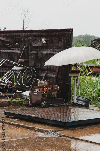 Industrial scales for weighing scrap metal under a grey umbrella on a rainy summer day.