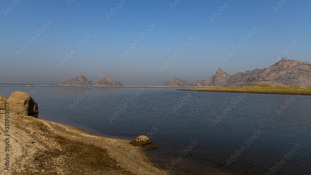 Fototapeta premium Landscape of Jawai dam with water, clear blue sky and Aravalli mountain ranges with its reflection in water at Jawai in Rajasthan India 