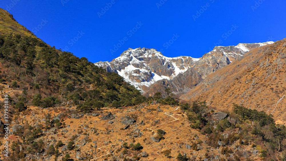 View of a valley with a narrow path leading up to the snow clad peaks in the distant at North Sikkim in India View of a valley with a narrow path leading up to the snow clad peaks in the distant at North Sikkim in India
