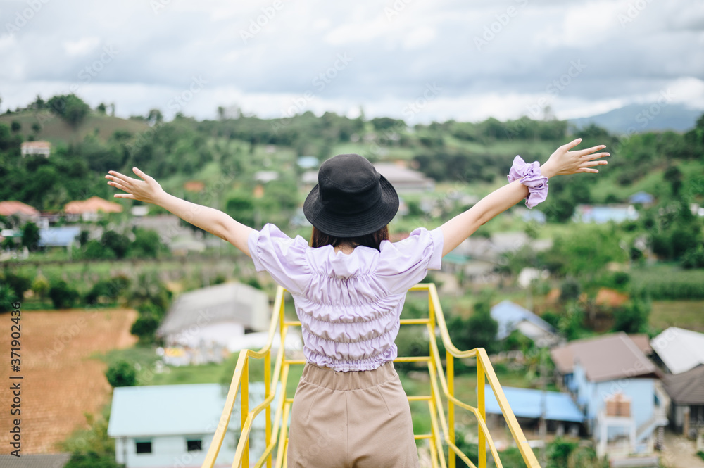 Back view of young Asian woman raised her hands when looking beautiful view of the nature and countryside village in Chiang Rai province of Thailand.