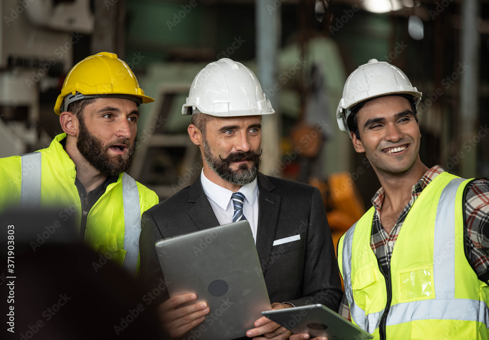 Factory manager in suit using laptop and talking with industrial engineer ,technician man. They wear helmet or hardhat with safety jackets inside industry manufacturing Facility/Discussion working Factory manager in suit using laptop and talking with industrial engineer ,technician man. They wear helmet or hardhat with safety jackets inside industry manufacturing Facility/Discussion working
