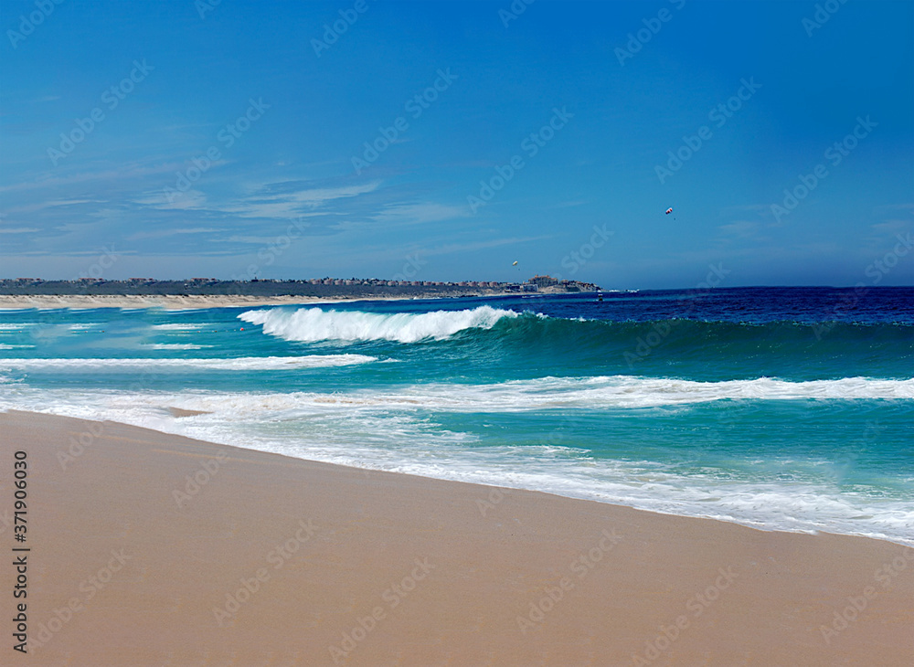 a dream vacation of white foam waves rolling on a sandy beach from a turquoise and deep blue ocean with a bright blue summer sky