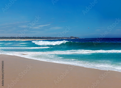 a dream vacation of white foam waves rolling on a sandy beach from a turquoise and deep blue ocean with a bright blue summer sky