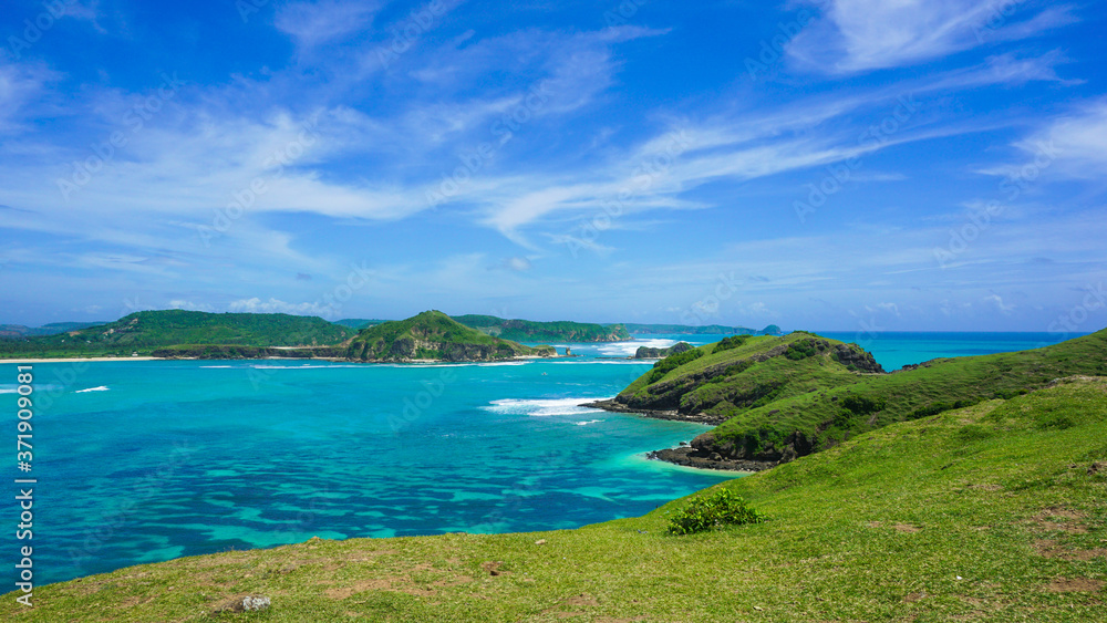 Green Hill at the Seashore in Bali with Emerald Colored Ocean, White Sand and Blue Sky