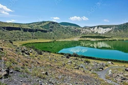 Beautiful mountain lake Nar. An emerald round-shaped reservoir in the crater of an extinct volcano. Summer sunny day, blue sky, light clouds. Reflection in water. Cappadocia. Turkey. 
