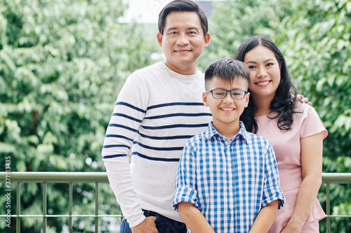 Portrait of happy Vietnamese family with preteen child standing outdoors and looking at camera