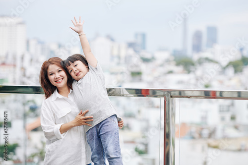 Portrait of joyful Vietnamese woman and her adorable little daughter standing on observation platform