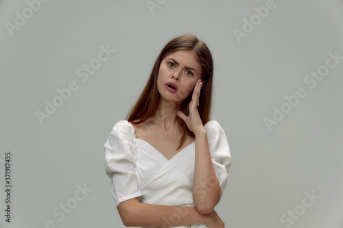 Surprised woman with open mouth holds hand near face white dress cropped 
