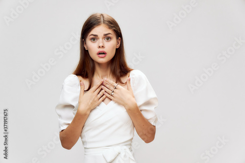 Surprised woman holding hands in front of her emotions white dress gray isolated background