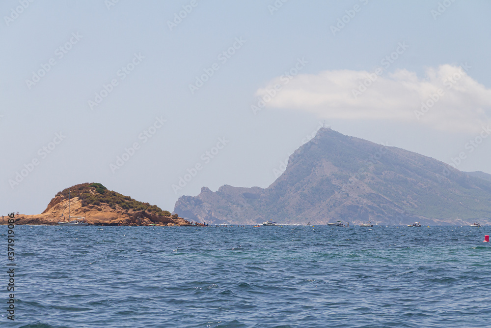 Island on the Mediterranean Sea and people enjoying a summer day of water sports and sports boats Alicante / Spain. In the background, a view of Punta Bombarda on the mountain of the Serra Gelada Natu