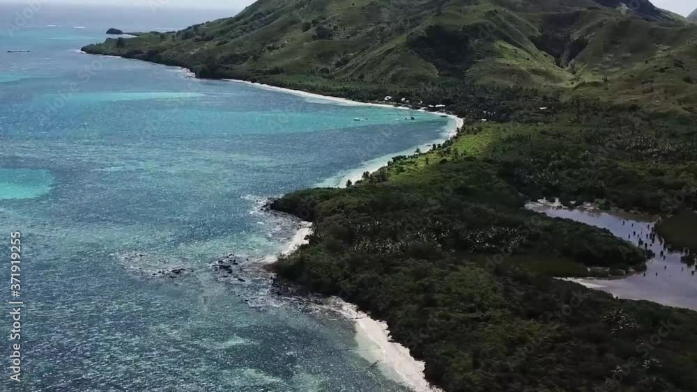 Flying over stunning ocean water with white sandy beach, pan up to dense green forest and green mountains Flying over stunning ocean water with white sandy beach, pan up to dense green forest and green mountains
