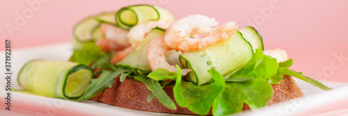 Open sandwich shrimp, cucumber, arugula. Homemade smorrebrod with rye bread. Pink background