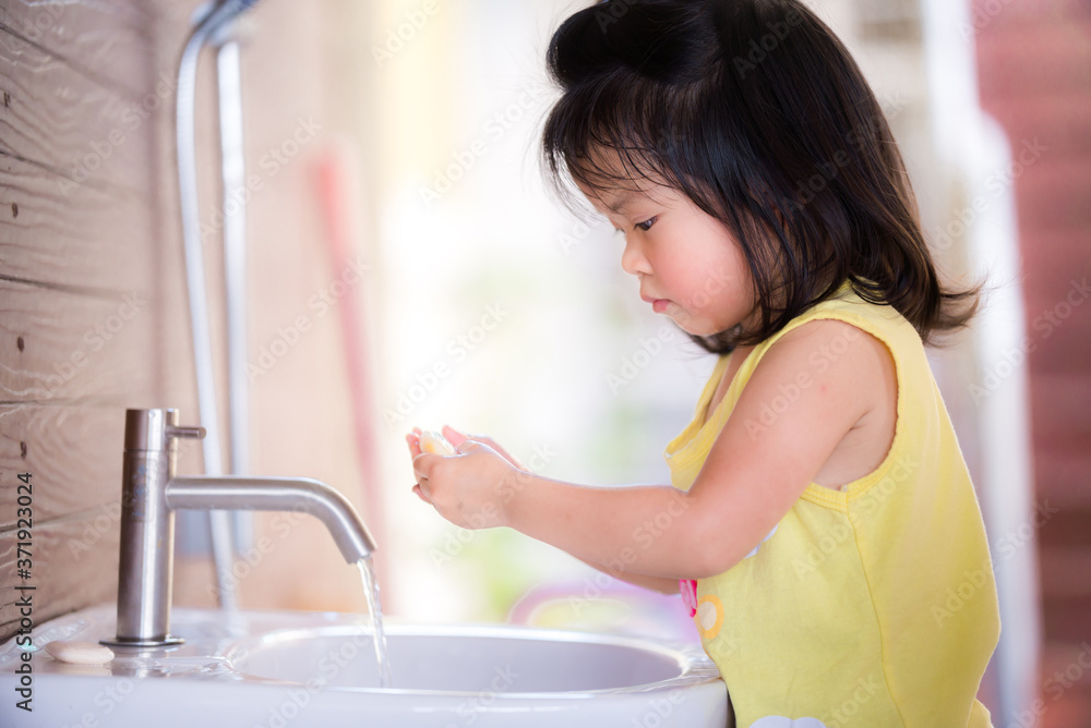 Adorable children wash their hands with soap in white sink. Asian kid is seriously cleaning her hands. She wear yellow shirt. Happy time for cleaning hands with water. Children are 3 years old. Adorable children wash their hands with soap in white sink. Asian kid is seriously cleaning her hands. She wear yellow shirt. Happy time for cleaning hands with water. Children are 3 years old.