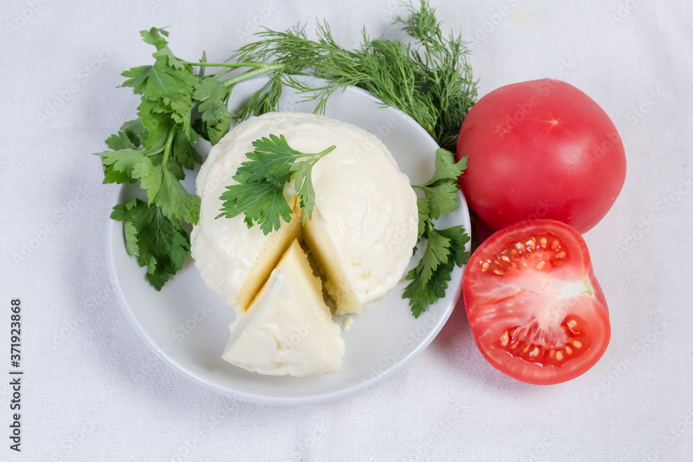 Soft cheese on saucer, tomatoes, greens on tablecloth, top view Soft cheese on saucer, tomatoes, greens on tablecloth, top view
