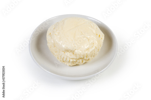 Small head of soft cheese on saucer on white background