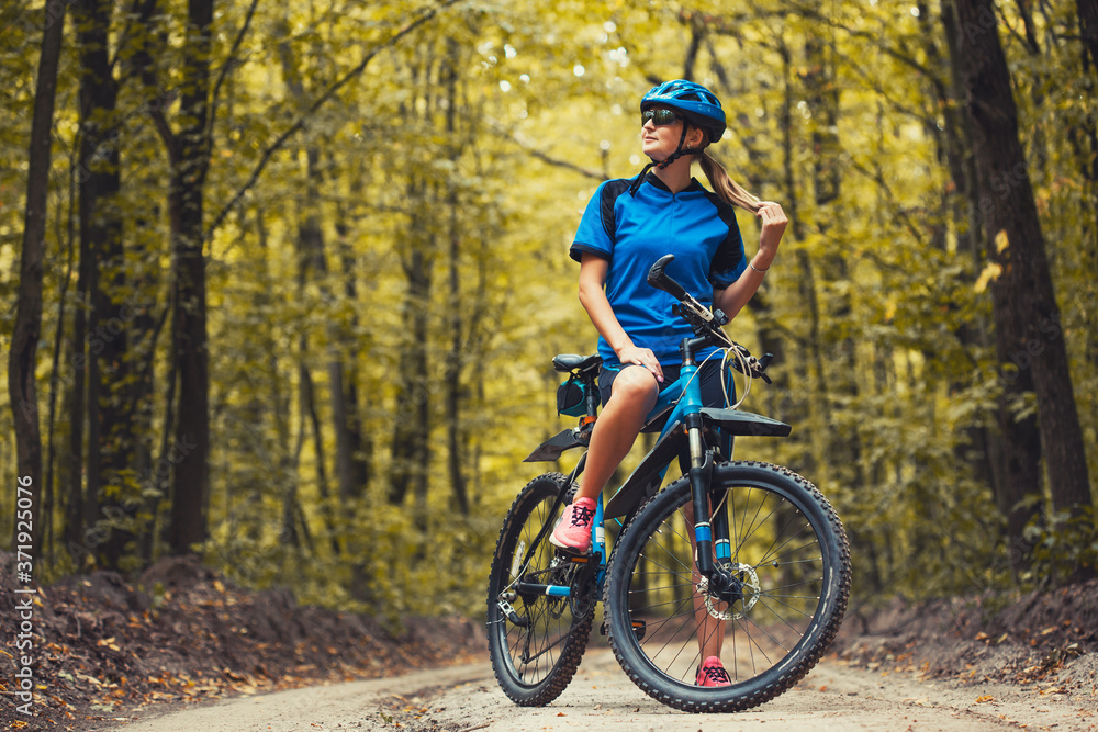 Fototapeta premium Caucasian woman cyclist rides mountain bike forest trails. leisure