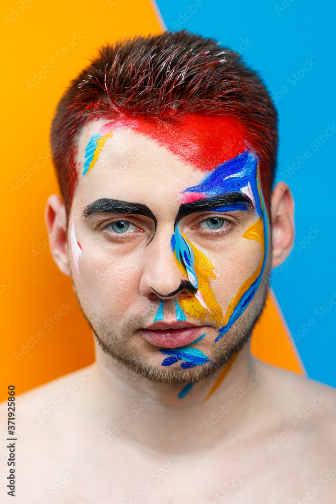 Makeup on the skin. Portrait of a young man with colored paint on a yellow background. Professional Makeup Fantasy Art Makeup