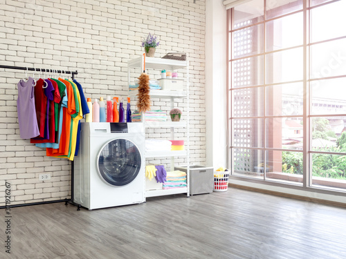 Laundry room interior with washing machine and colorful clothes on white vintage brick wall background.