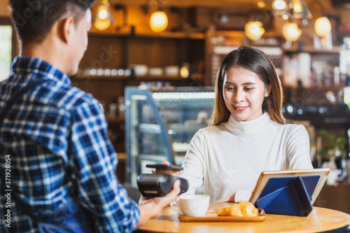 Asian customer man paying with credit card via contactless nfs technology to Asian Barista of Small business owner at the table in coffee shop  Small business owner and startup in coffee shop concept