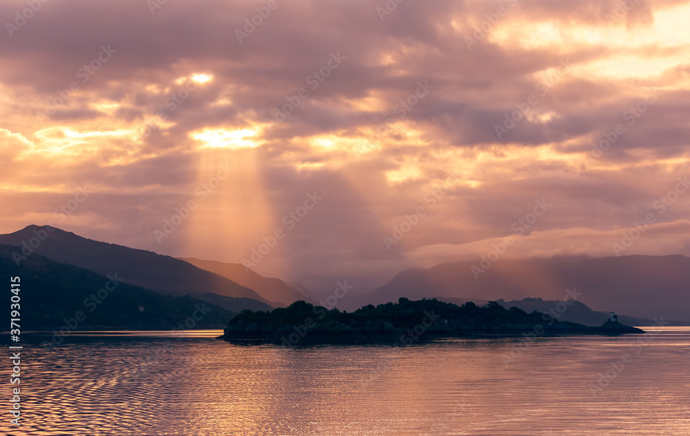 Sunrise in the Inner Hebrides, Scotland, with sunrays bursting through the clouds on the mountain range.  Concept: Tranquility.  Horizontal.  Space for copy.