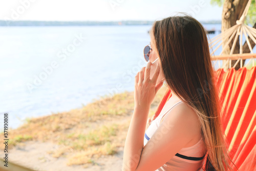 Young woman talking by phone while relaxing in hammock outdoors