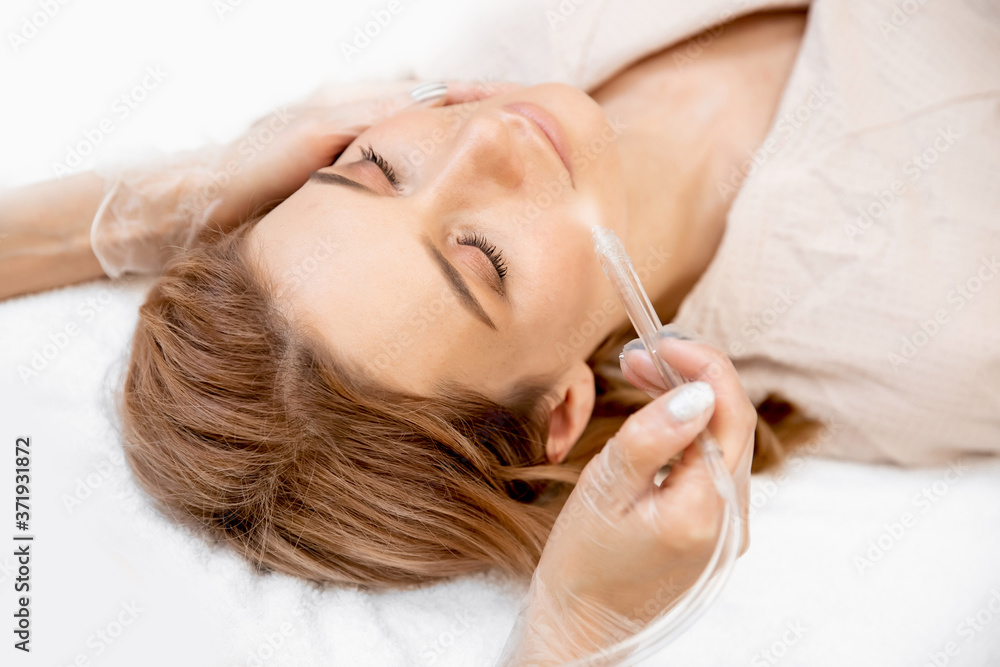 Fototapeta premium Procedure wet cleaning skin of face from blackheads, acne of young woman in clinic