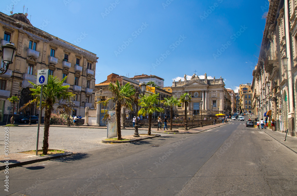 Italy, Catania, May 13, 2018: view of Roman Amphitheater ruins and Chiesa San Biagio in Sant'Agata alla Fornace catholic church near Piazza Stesicoro square and street with palms, Sicily