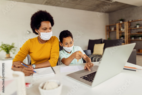 Black mother and son with face masks using laptop while homeschooling. © Drazen