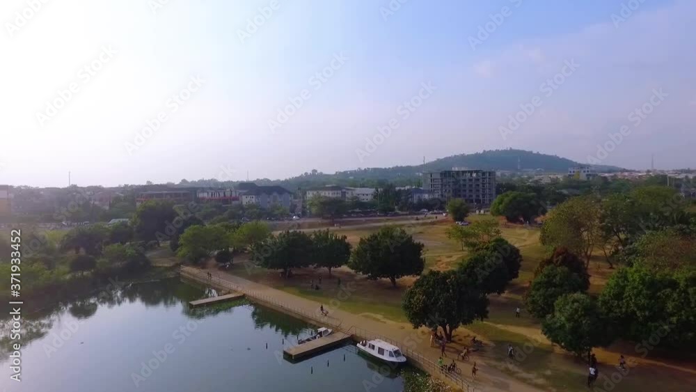 Aerial view overlooking a boat at a pier, a man made lake and the Jabi Recreational Park, sunny evening, in Abuja, Nigeria - reverse, drone shot Aerial view overlooking a boat at a pier, a man made lake and the Jabi Recreational Park, sunny evening, in Abuja, Nigeria - reverse, drone shot